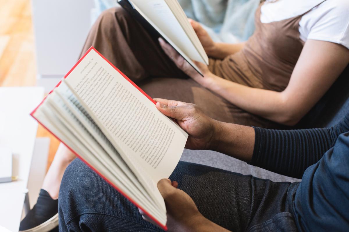 Two people are reading books while sitting side by side.